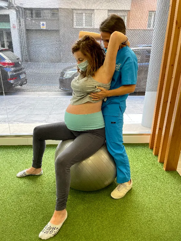 Nuestra físio Paula ayundando a realizar un ejercicio a una embarazada sentada en una pelota grande